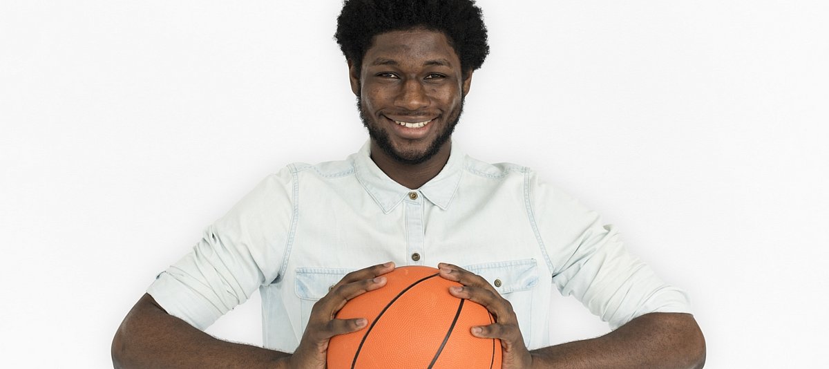 Ein junger Mann mit dunkler Hautfarbe hält einen Basketball in der Hand und lächelt