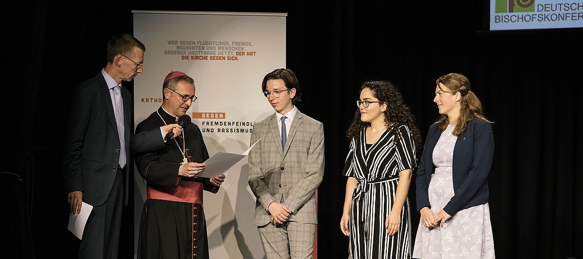 Erzbischof Stefan Heße und drei Preisträger/-innen des Projekts „Tacheles!“ von KLJB und BDAJ stehen gemeinsam auf einer Bühne.