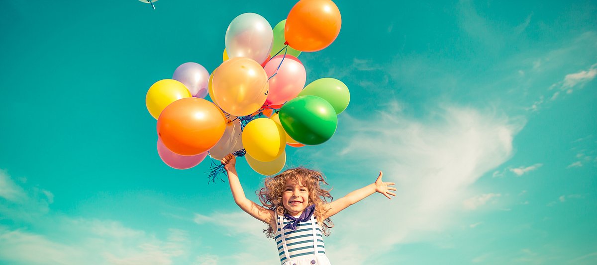 Kind mit Luftballons hüpft in die Luft