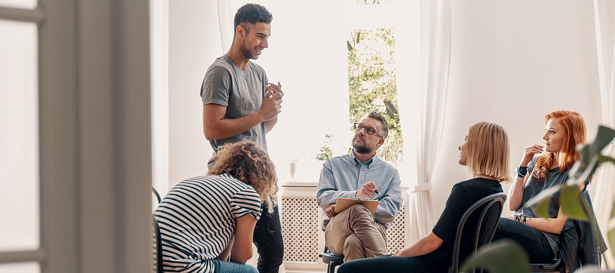 Vier junge Erwachsene unterschiedlicher Herkunft sprechen entspannt im Kreis mit einem Mann