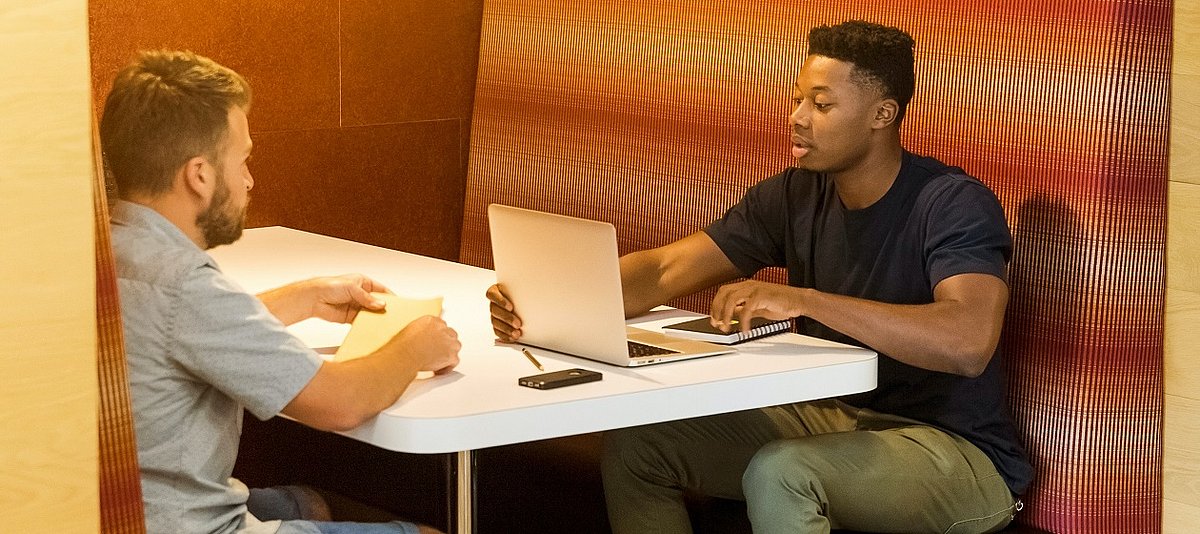 Zwei Männer mit Notizen und Laptop besprechen sich an einem Tisch