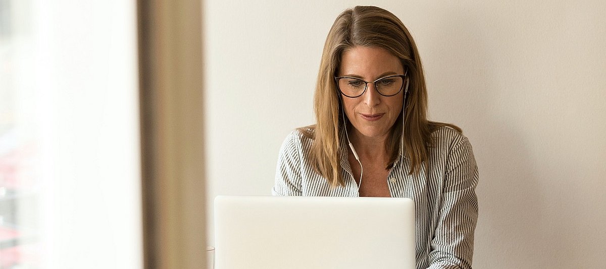 Frau mit Kopfhörern sitzt vor Laptop und scheint digital zu arbeiten