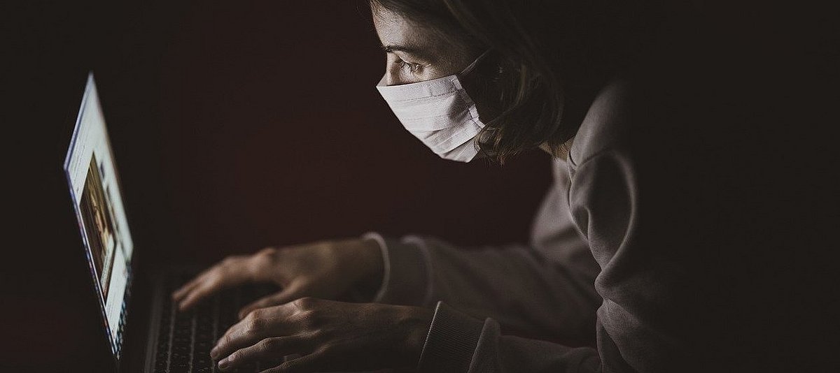 Eine junge Frau mit Maske sitzt im Dunkeln vor einem Laptop