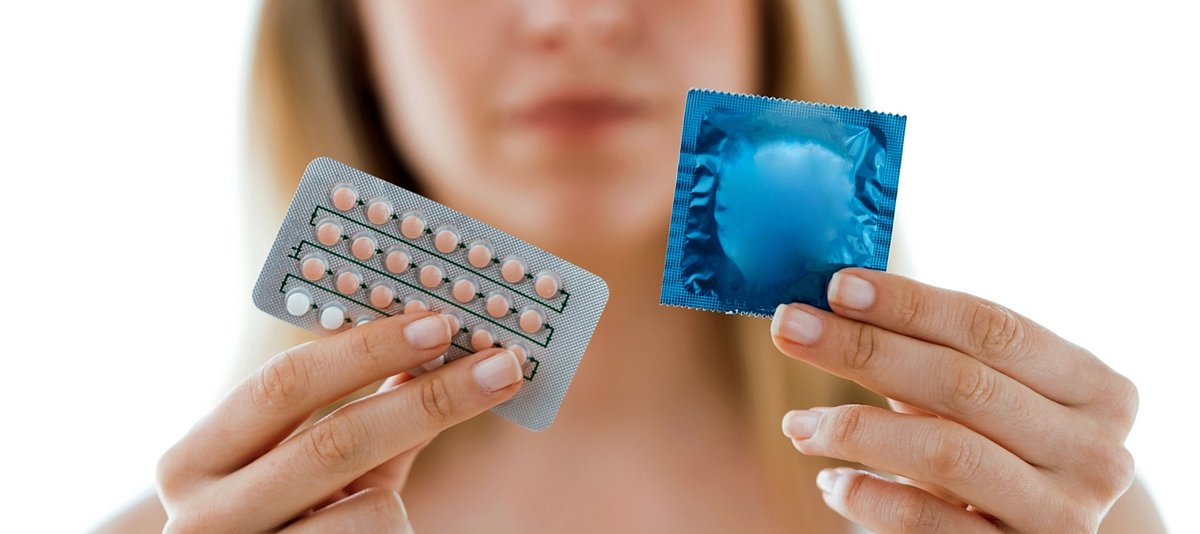 Eine Frau hält in jeweils einer Hand eine Pillen-Packung und ein Kondom hoch