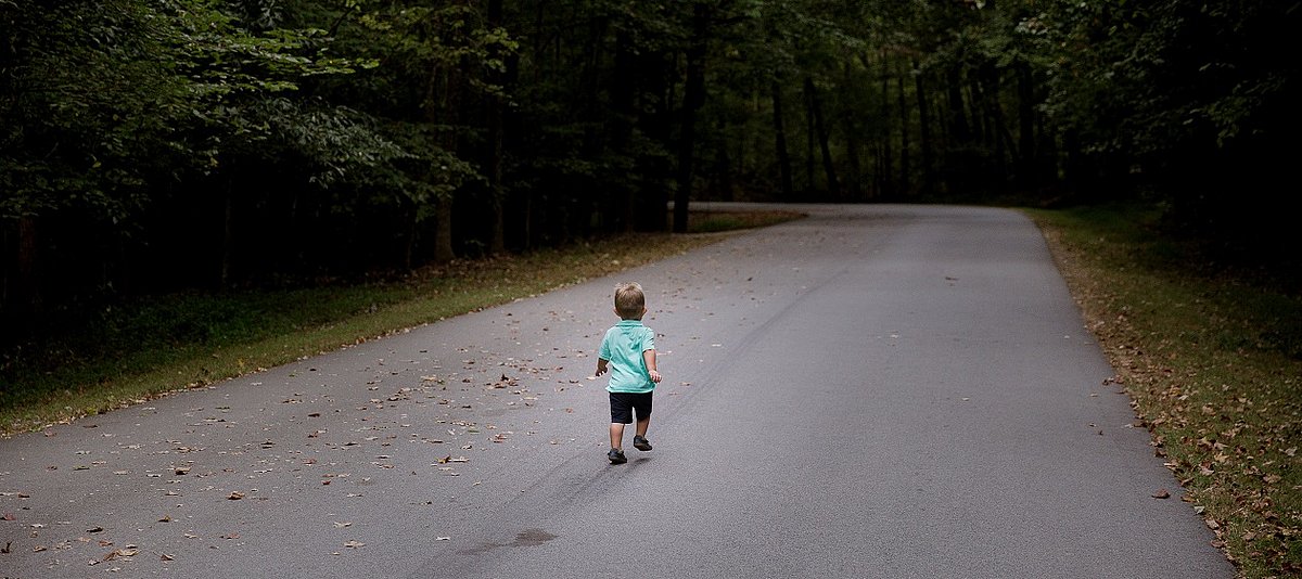 Ein Kleinkind geht auf einer leeren Straße, die von Wald umgeben ist