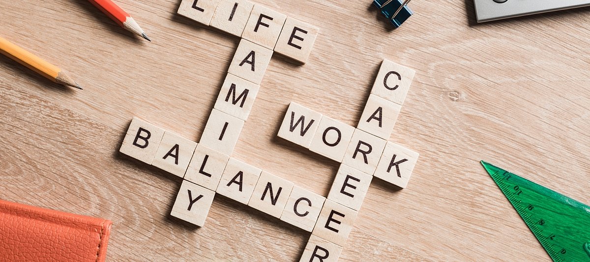Die englischen Worte work, life, balance, family und career liegen durch Holzsteine gebildet auf einem Tischn