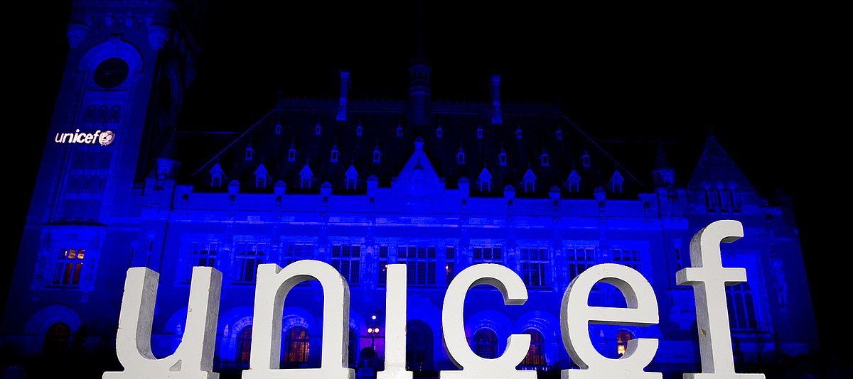 Gebäude wird blau angestrahlt, davor steht eine Skulptur mit den Buschtaben UNICEF