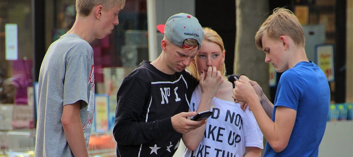 Vier Teenager stehen zusammen in einer Einkaufsstraße und zwe davin schauen auf ihre Smartphones
