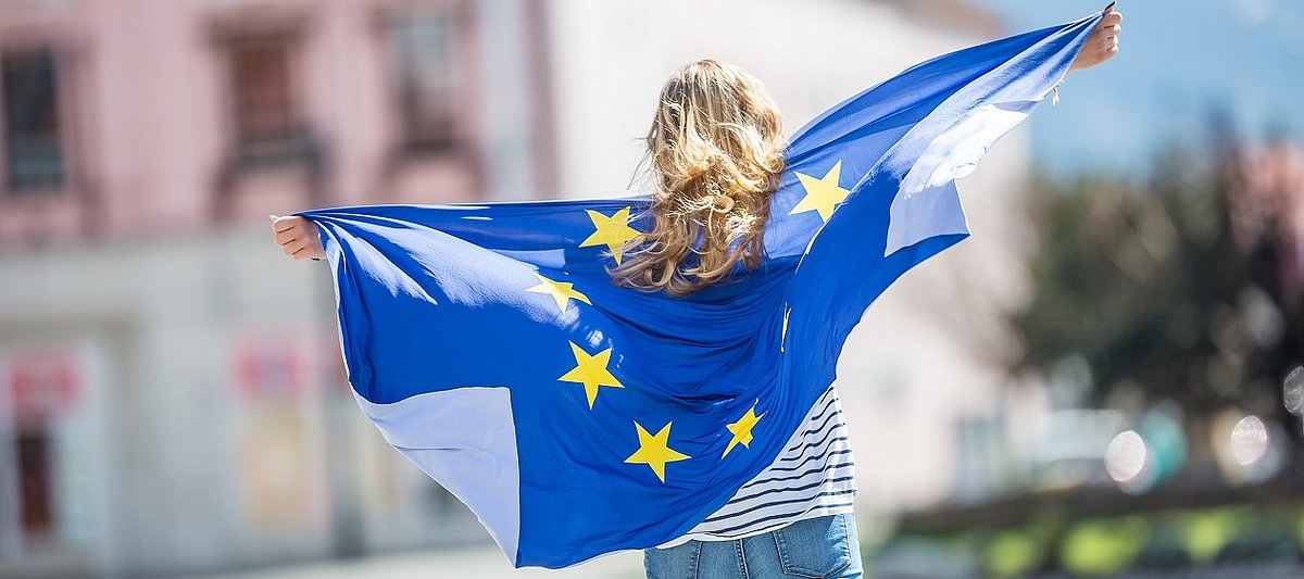 Eine Jugendliche hält eine Europaflagge hinter sich ausgebreitet
