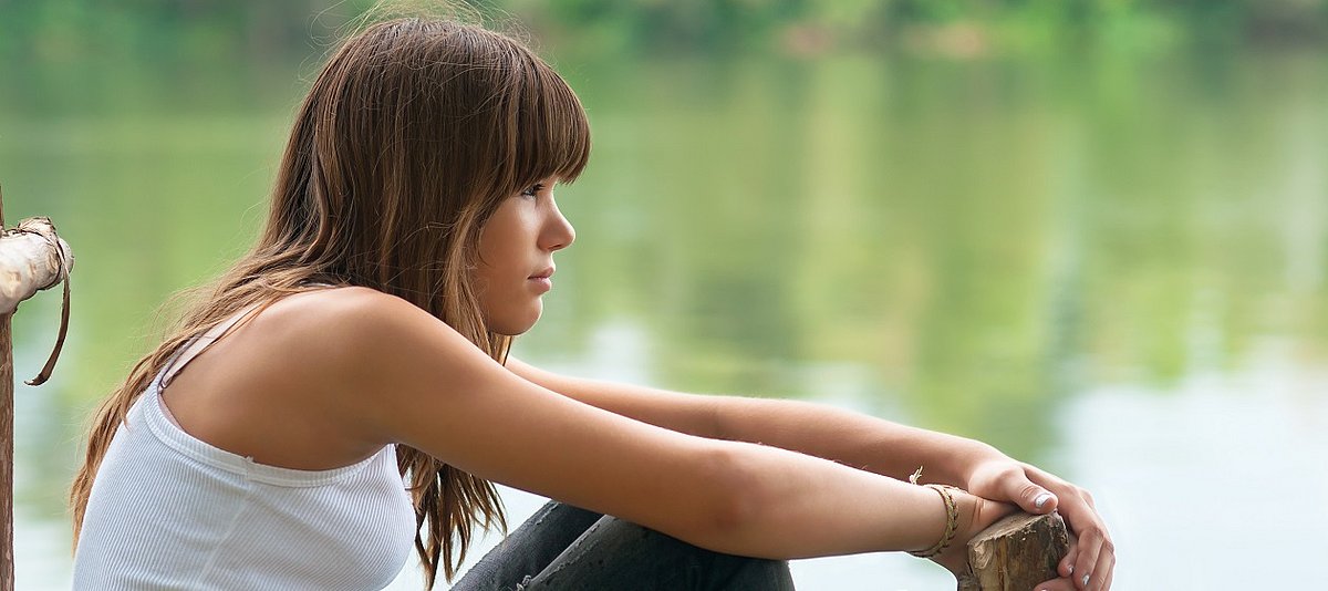ein Mädchen sitzt mit nachdenklichem Blick am Ufer