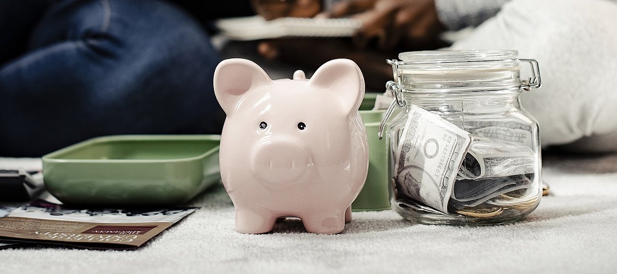 Ein Sparschwein steht neben einem Einmachglas, in dem viele Geldscheine sind