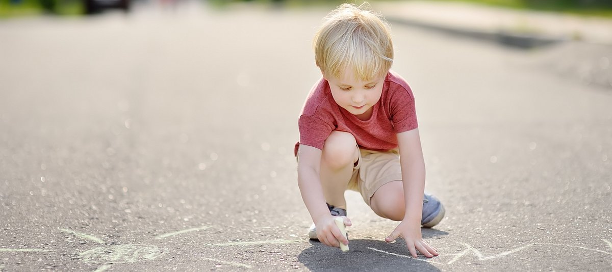 Eine Junge malt im Sommer mit Kreide auf dem Asphalt