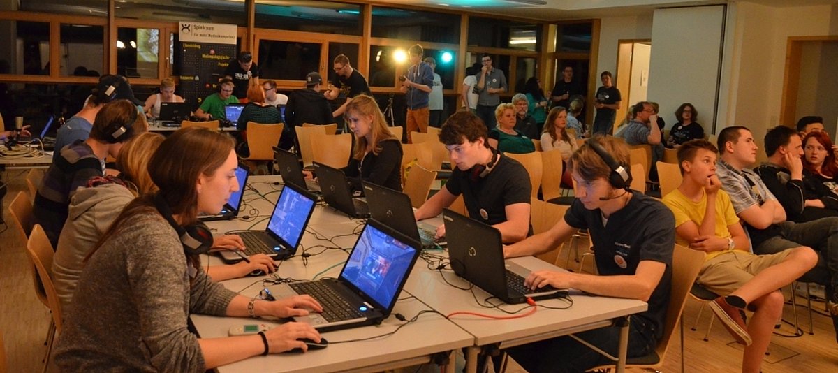 Viele Jugendliche sitzen mit Laptops an zwei Tischreihen