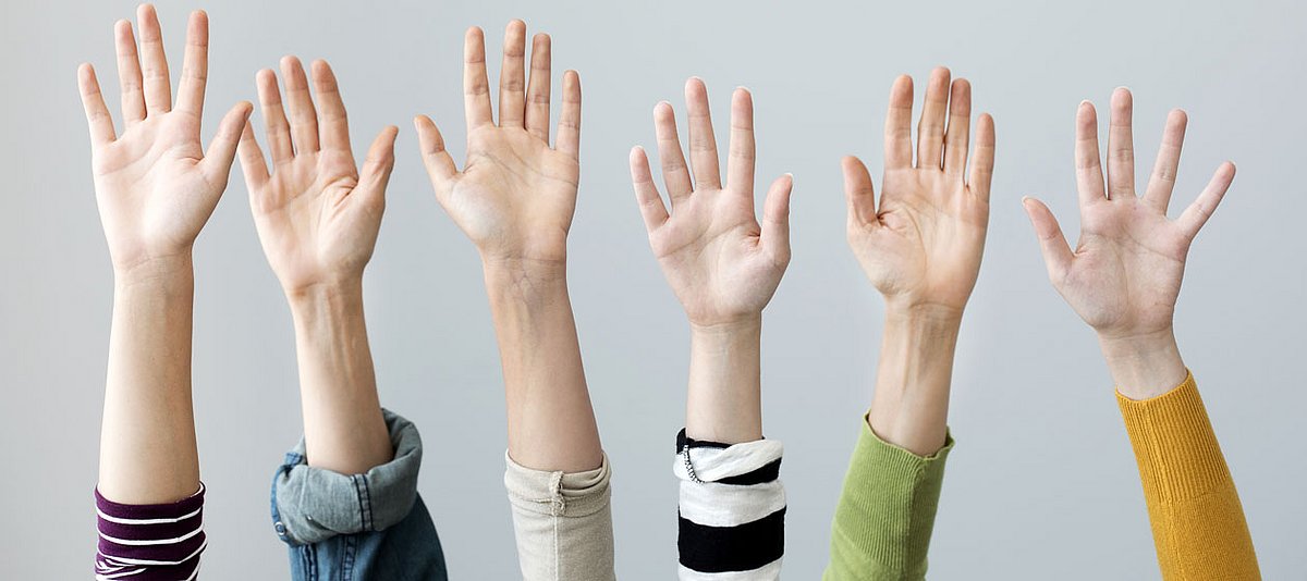 Sechs Hände von Jugendlichen sind nach oben gestreckt, wie bei einer Abstimmung.