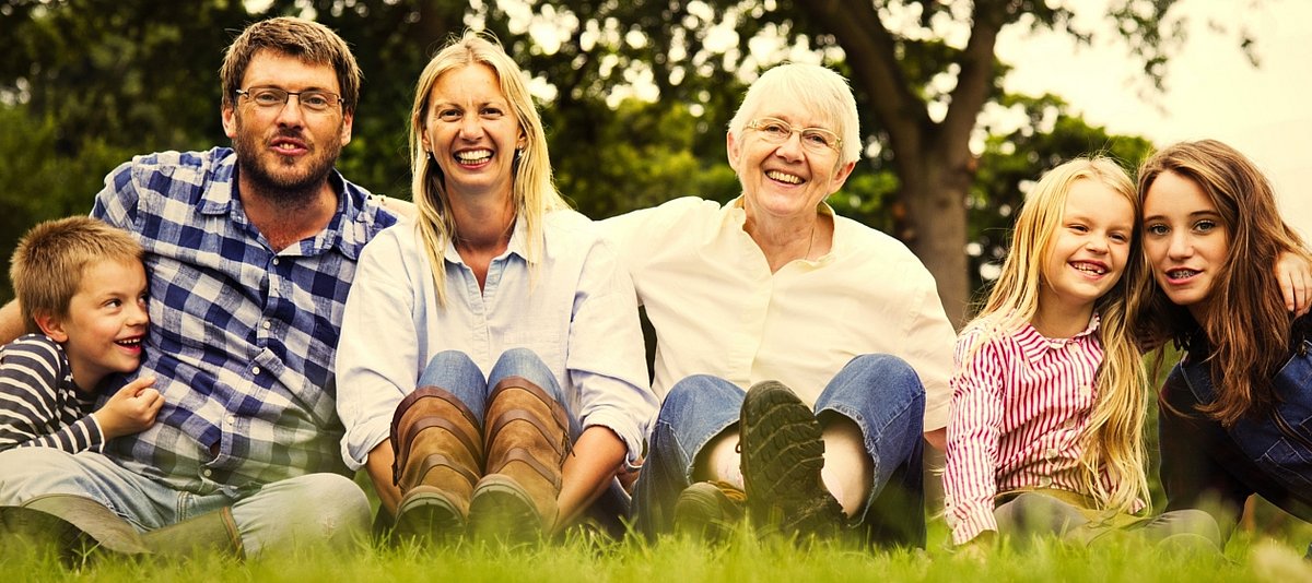 Eine Familie mit Großmutter und Enkeln sitzt im Gras und lacht in die Kamera