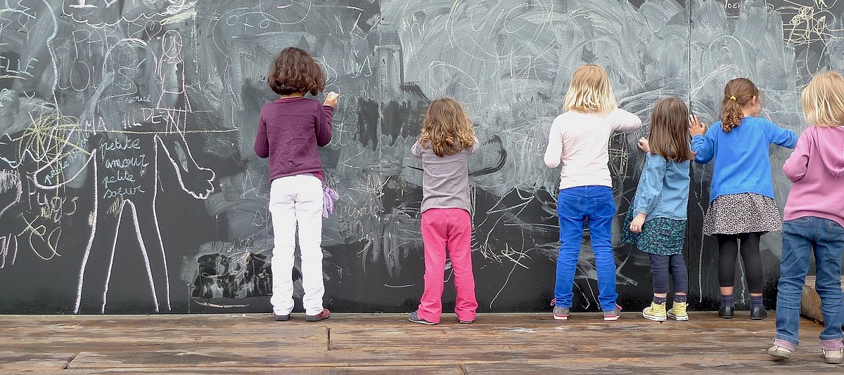Eine gruppe von Kindern steht vor einer Wand und bemalt diese mit Kreide.