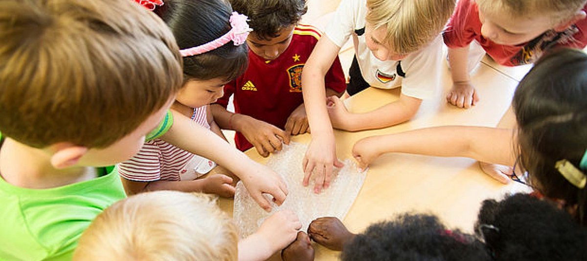 Eine Gruppe Kinder mit unterschiedlicher Hautfarbe schauen sich etwas gemeinsam an einem Tisch an