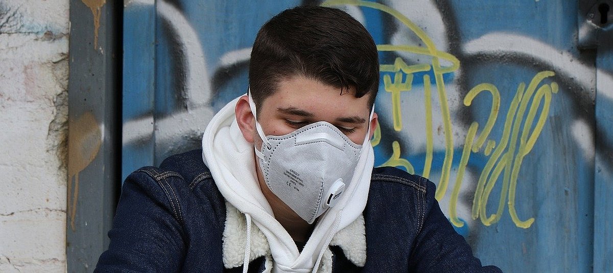 Jugendlicher mit Atemschutzmaske schaut zu Boden