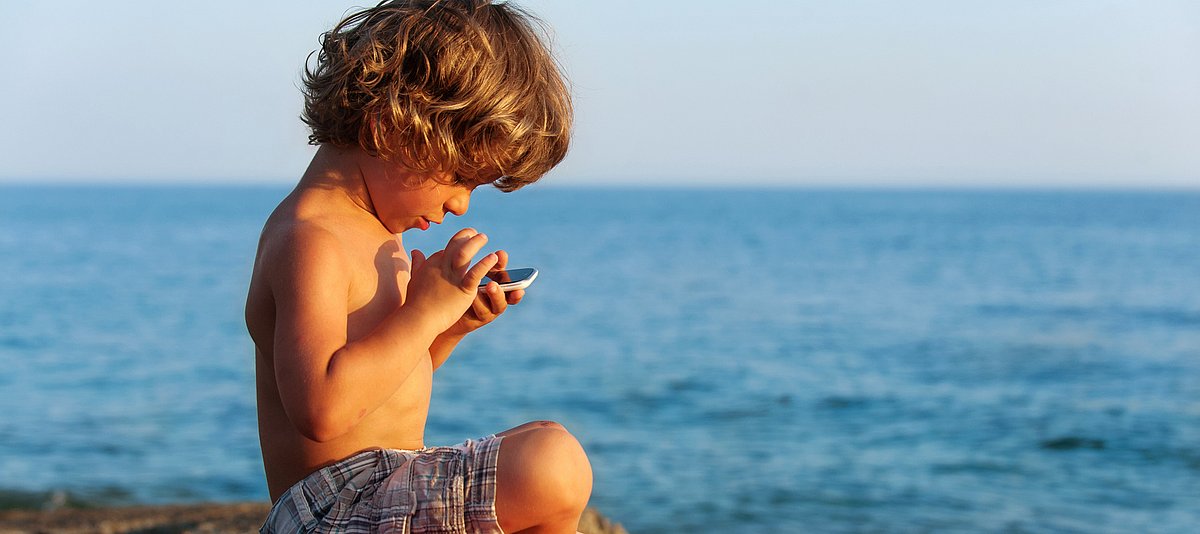 Kind am Meer spielt mit Smartphone
