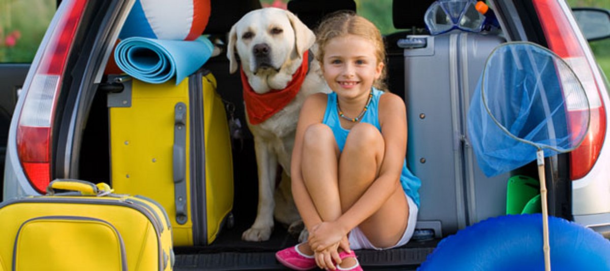 Ein Mädchen und ein Hund warten im Auto auf die Abreise in den Urlaub