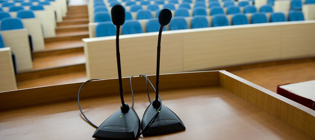 Auf dem Podium eines Hörsaals stehen Mikrofone.