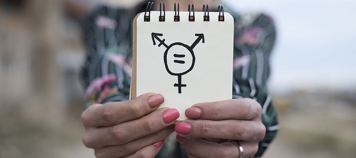 Eine Person hält einen Notizzettel in der Hand, darauf ist das Transgender-Symbol zu sehen