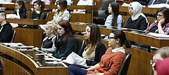 Junge Menschen sitzen als Abgeordnete in einem Parlamentsplenum und lauschen der Debatte.