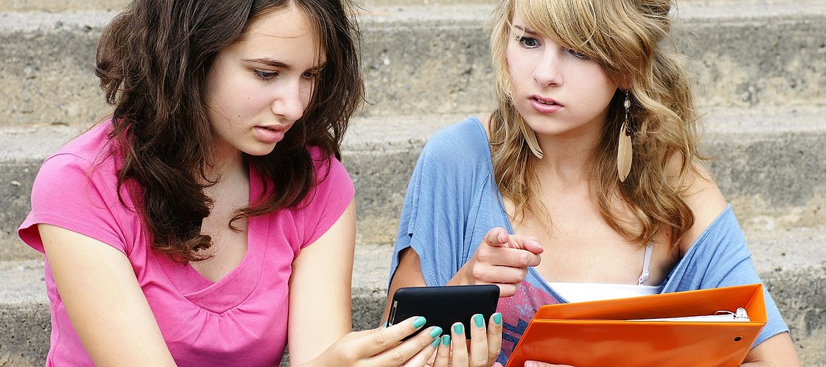 zwei Mädchen sitzen auf der Treppe und schauen auf ein Handy