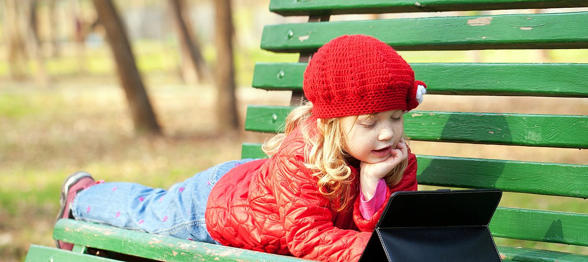 Kind liegt auf Parkbank mit Tablet