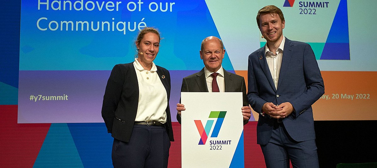 Y7 Co-Vorsitzende Coralina Claus und Benjamin Günter mit Bundeskanzler Olaf Scholz auf der Bühne des Y7-Jugendgipfels.