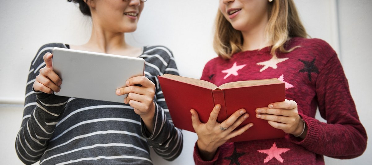 Zwei Jugendliche lesen auf einem Tablet und in einem Buch
