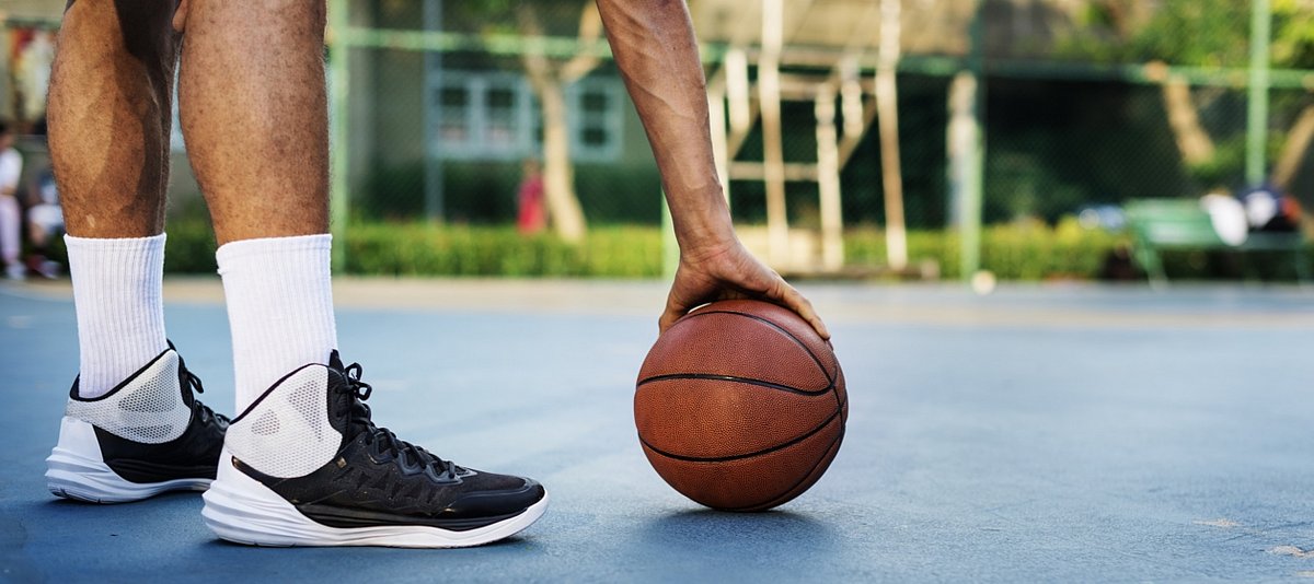 Ein junger Mensch steht auf einem Basektballplatz in der Stadt und ein Basketball liegt vor ihm auf dem Boden