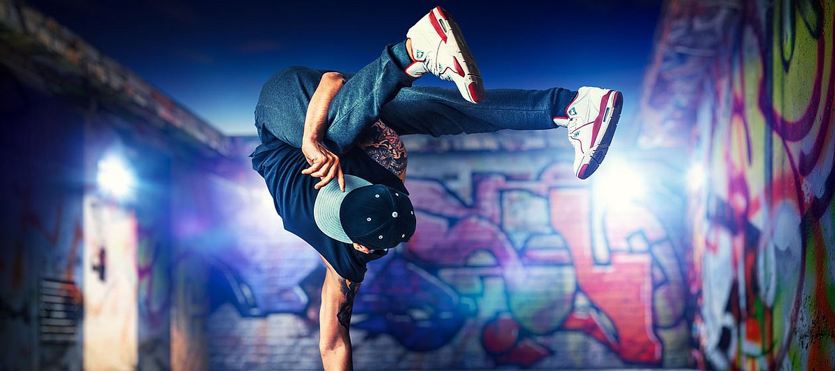 Einer junger Mann macht Breakdance vor einer Wand mit Graffiti.  