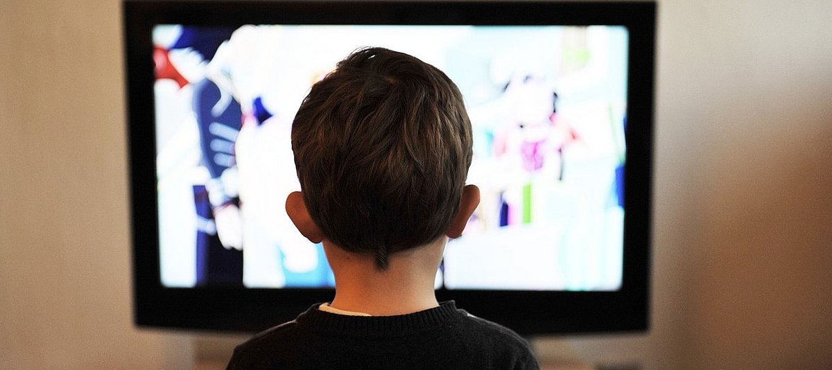 Ein Kind schaut Fernsehen, das Kind ist von hinten zu sehen