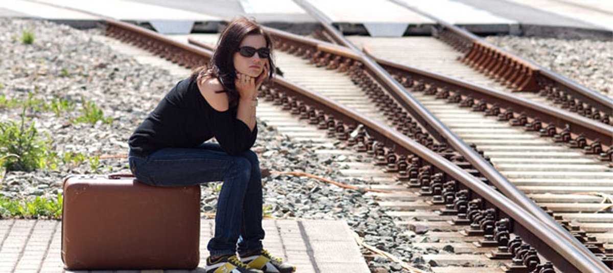 Eine junge Frau sitzt auf ihrem Koffer an den Bahngleisen