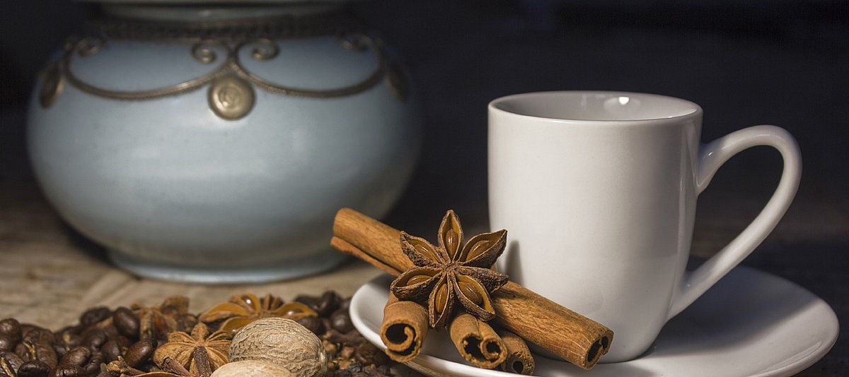 Eine Kaffeetasse mit Zimtstangen, Anis und Muskatnuss auf einem braunen Holztisch