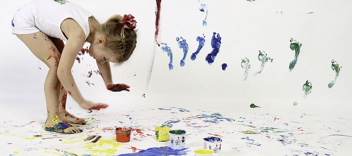 Ein Mädchen gestaltet mit Fingerfarben ein großflächiges Bild.