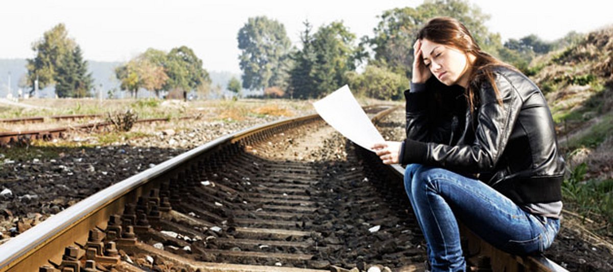 Eine junge Frau sitzt auf den Bahngleisen
