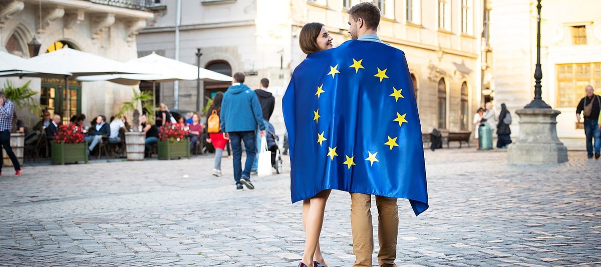 Ein Paar auf einem Platz hat sich gemeinsam eine Europafahne um die Schultern gelegt