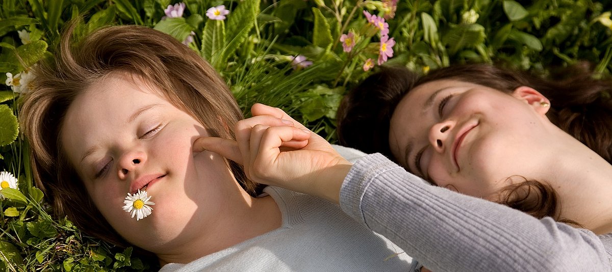 Zwei Kinder liegen auf einer Blumenwiese und spielen miteinander.