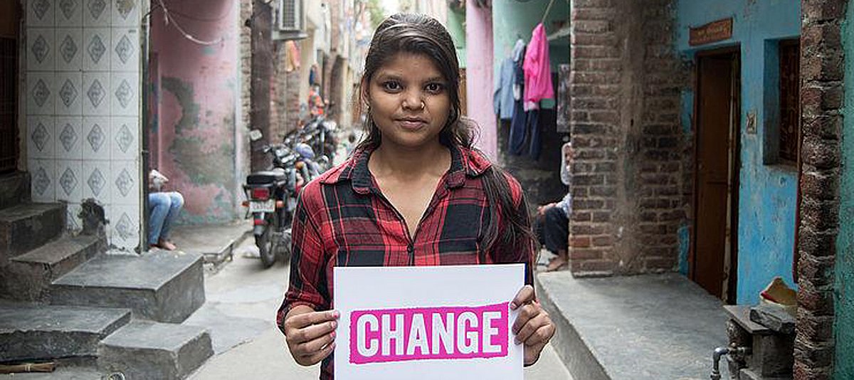 Eine junge Frau steht in einer Straße und hält ein Schild mit der Aufschrift "Change". 