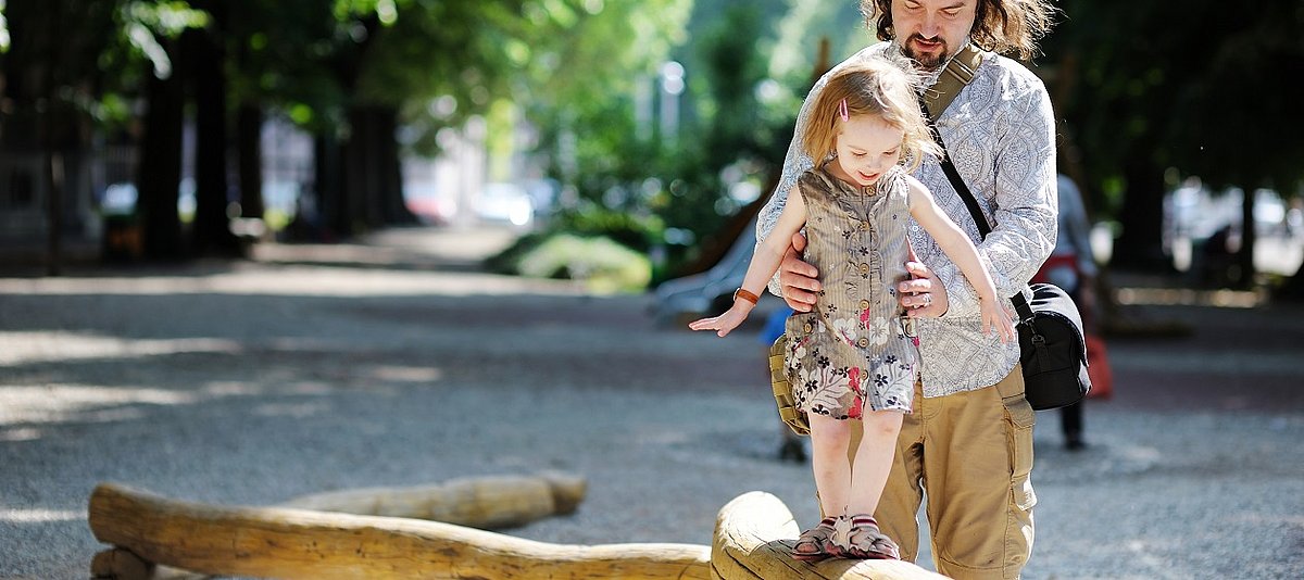 Mann hilft kleinem Mädchen beim Balancieren auf einem Baumstamm