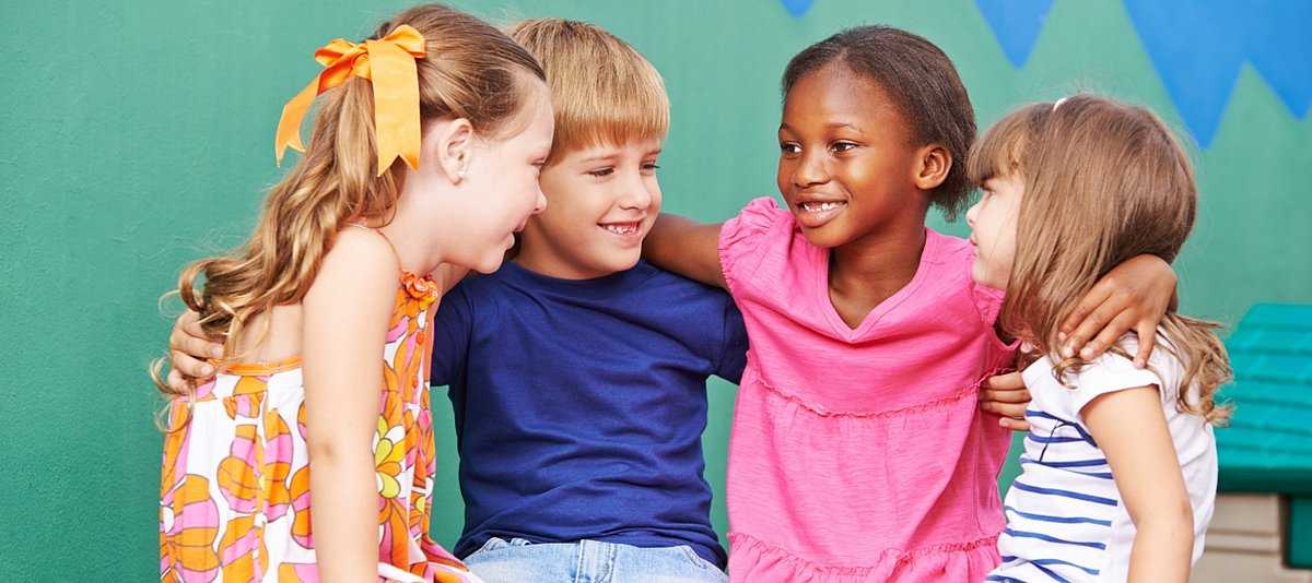 Vier Kindermit unterschiedlicher Hautfarbe umarmen sich