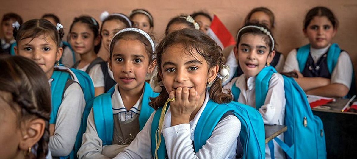 Fröhliche Mädchen sitzen an ihren Tischen im Klassenzimmer ihrer Schule im Irak. 