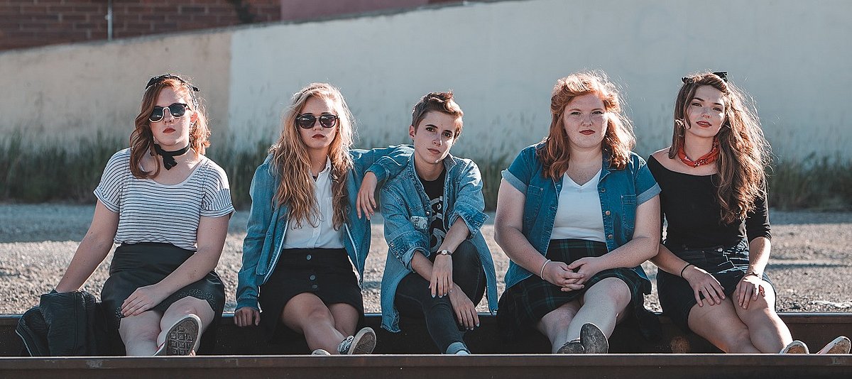Fünf junge Frauen sitzen auf einem alten Bahngleis und schauen in die Kamera