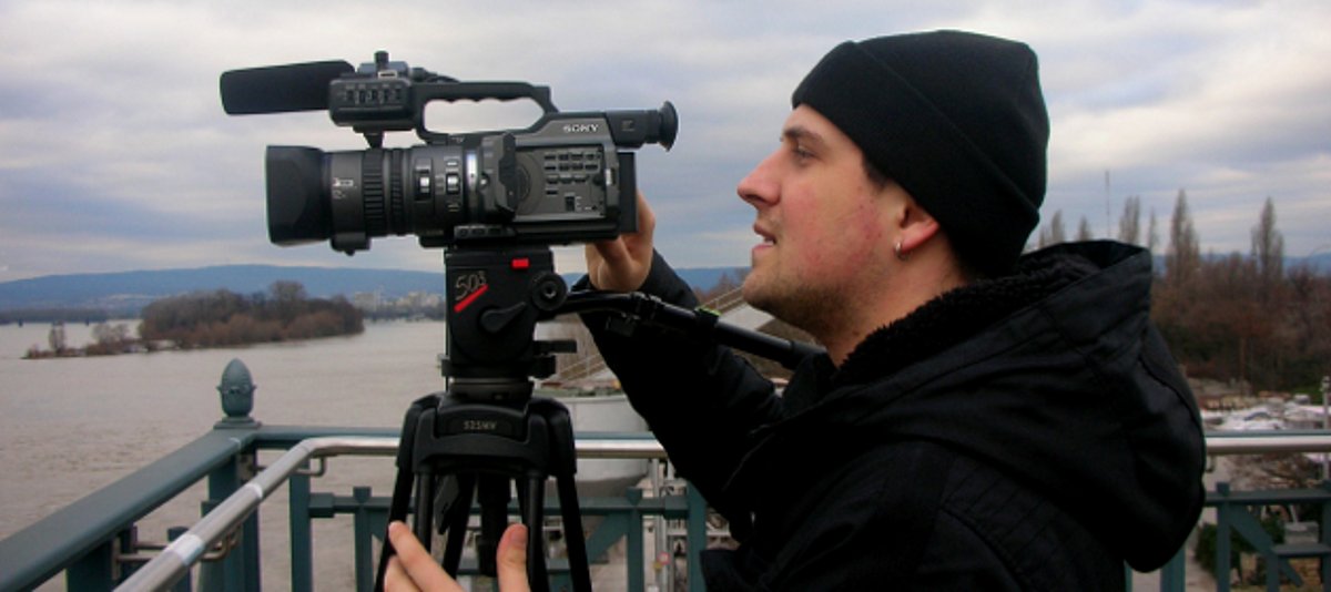 Ein junger Mann steht hinter einer Videokamera und filmt.