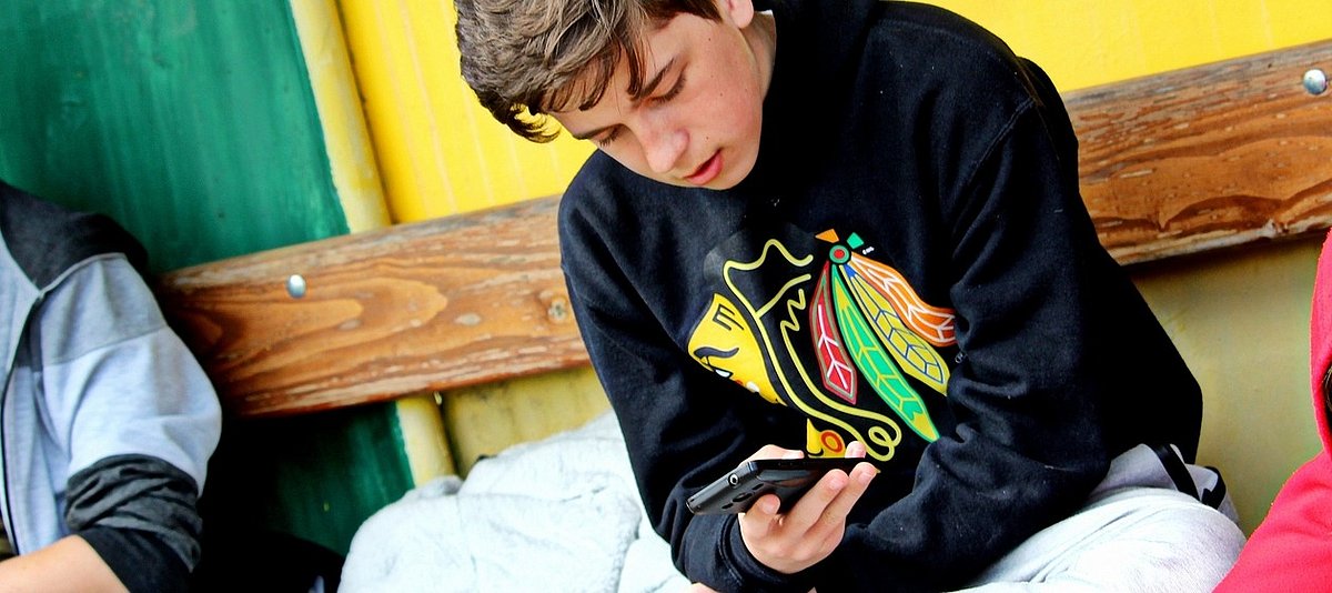 Auf dem Bild ist ein Jugendlicher mit einem Handy zu sehen.