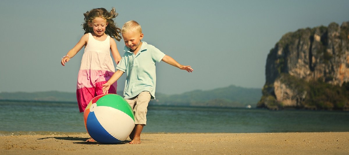 Zwei Kinder spielen am Strand ausgelassen mit einem Ball 