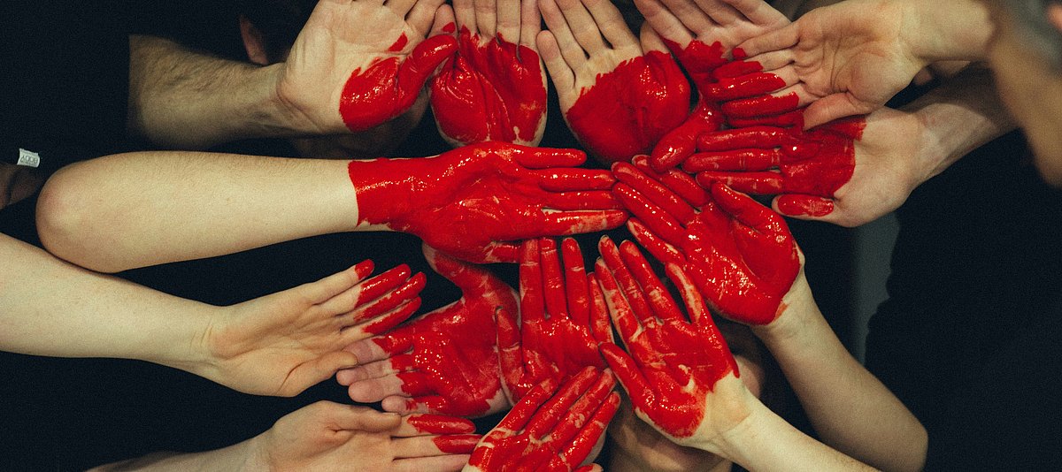 Hände, die zusammen mit roter Herzfarbe geformt wurden
