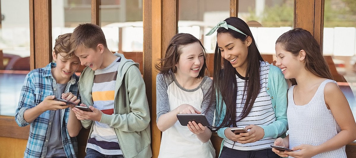 Fünf Jugendliche stehen nebeneinander und zeigen sich Dinge auf ihren Smartphones